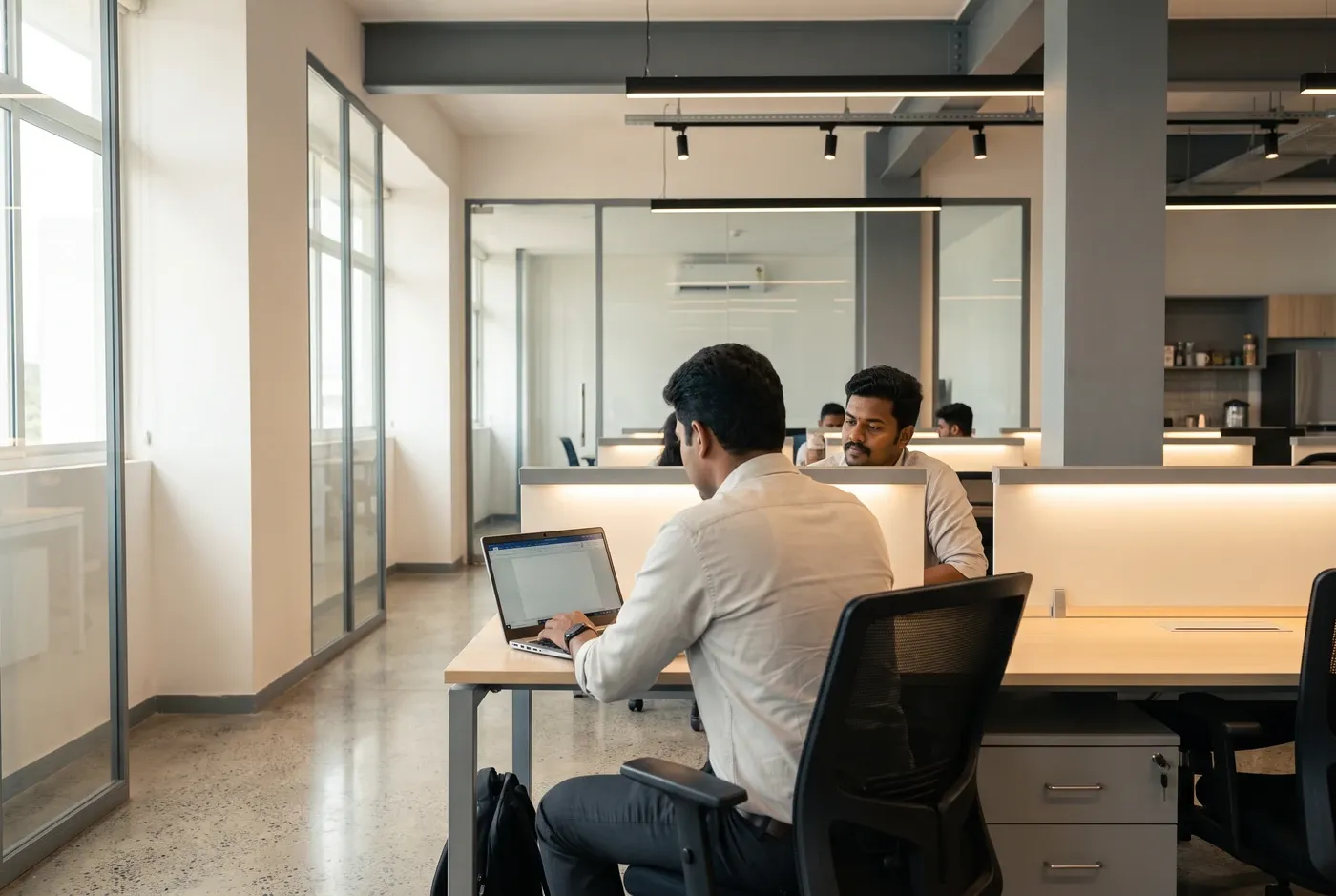Two colleagues at a desk, one presenting to a laptop