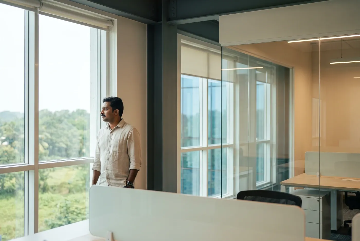 A single figure standing at a tall window in a dark office